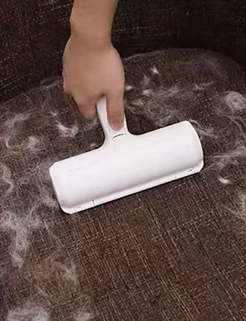 Pet hair roller being rolled over a fabric couch covered in shed hair